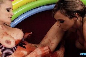 Big titty lesbians are rubbing on their clits in a pool filled with red jello